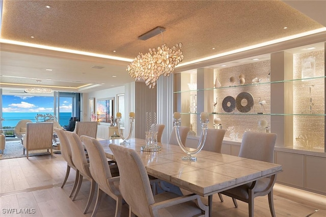 dining space featuring a textured ceiling, a tray ceiling, light wood finished floors, and a chandelier
