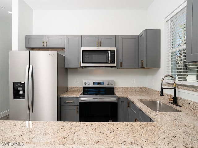 kitchen with light stone countertops, gray cabinetry, stainless steel appliances, and a sink