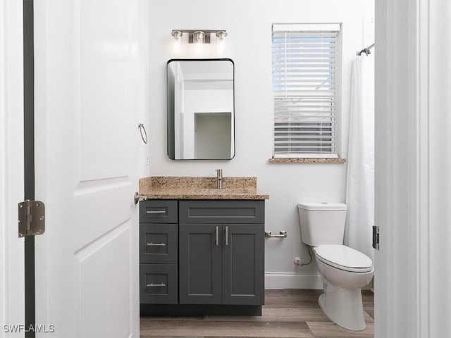 bathroom with toilet, vanity, baseboards, and wood finished floors