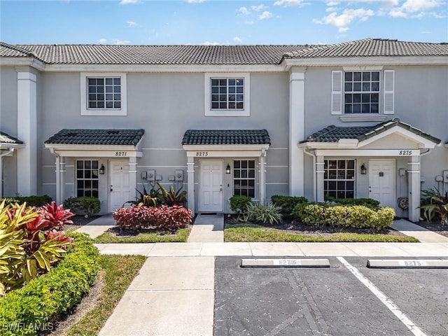 multi unit property featuring stucco siding, a tile roof, and uncovered parking