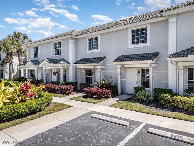 multi unit property with stucco siding, a tile roof, and uncovered parking