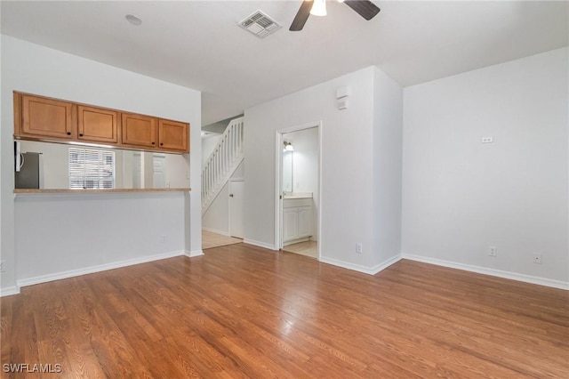 unfurnished living room featuring visible vents, wood finished floors, ceiling fan, and stairway