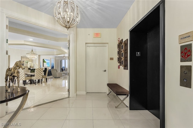 hallway featuring elevator, light tile patterned flooring, crown molding, a raised ceiling, and a chandelier