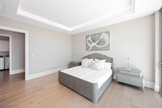 1165 8th St S Unit 202, Naples, FL 34102 - bedroom with baseboards, a tray ceiling, light wood-style flooring, and separate washer and dryer