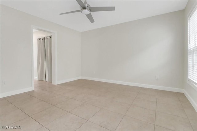 spare room with light tile patterned floors, a ceiling fan, baseboards, and a wealth of natural light