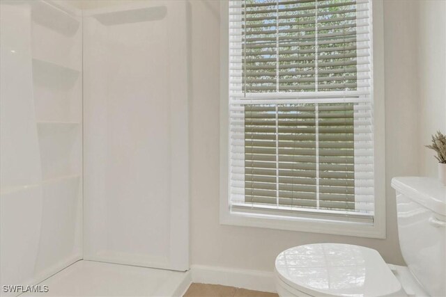 bathroom featuring toilet, baseboards, and walk in shower