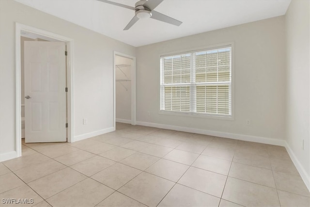 unfurnished bedroom with a walk in closet, baseboards, light tile patterned flooring, and a ceiling fan