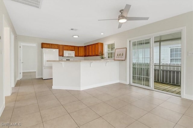 kitchen with brown cabinets, white appliances, a peninsula, light countertops, and light tile patterned floors