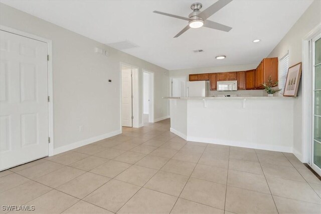 kitchen with white appliances, a peninsula, ceiling fan, light countertops, and brown cabinets