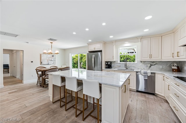 kitchen featuring visible vents, light wood-type flooring, a kitchen island, stainless steel appliances, and tasteful backsplash