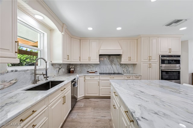 kitchen with visible vents, decorative backsplash, custom exhaust hood, black appliances, and a sink
