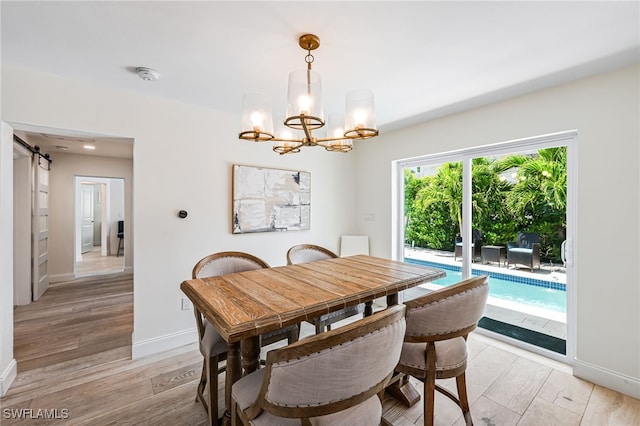 dining room with a barn door, a notable chandelier, baseboards, and light wood-style floors
