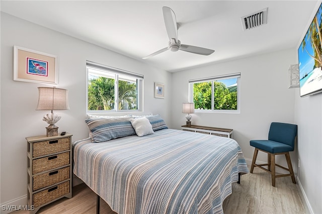 bedroom with multiple windows, wood finished floors, visible vents, and baseboards