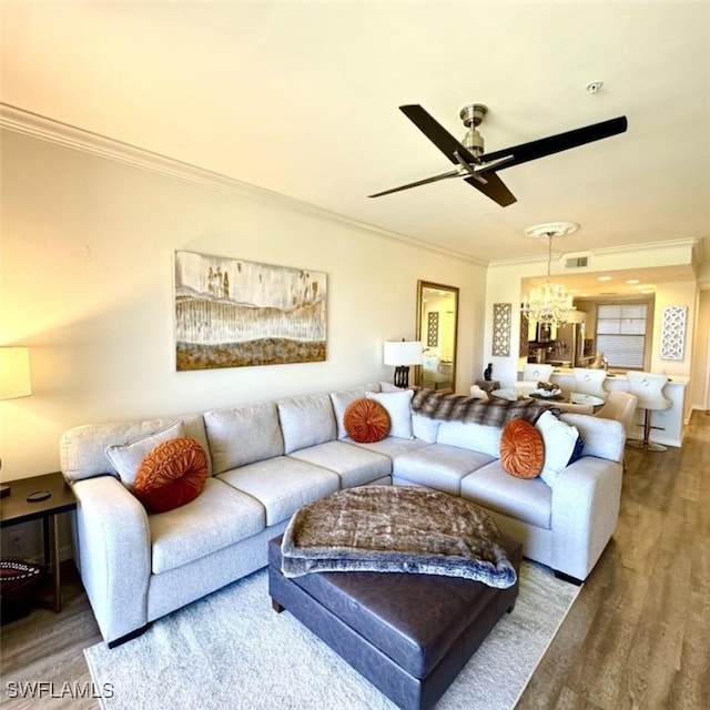 living room with visible vents, wood finished floors, ornamental molding, and ceiling fan with notable chandelier