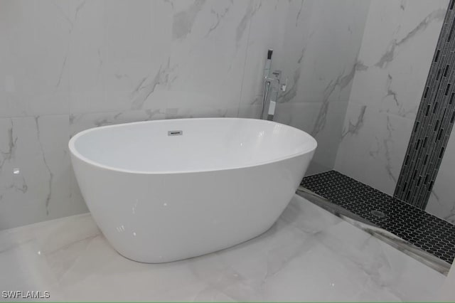 full bath with marble finish floor, a freestanding bath, and stone wall