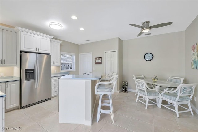 41 5th St, Bonita Springs, FL 34134 - kitchen with stainless steel fridge, light tile patterned floors, a ceiling fan, a kitchen bar, and white cabinets