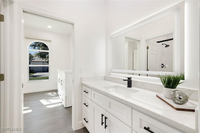 bathroom featuring vanity, wood finished floors, baseboards, and walk in shower