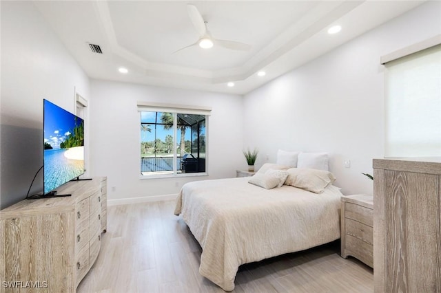 bedroom featuring light wood-type flooring, visible vents, a tray ceiling, recessed lighting, and baseboards