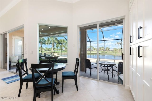 dining space with light tile patterned floors, a water view, baseboards, and a sunroom