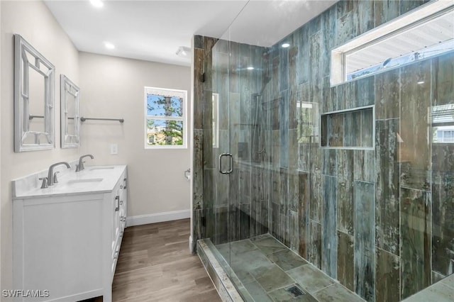 bathroom featuring baseboards, a sink, a stall shower, double vanity, and wood finished floors