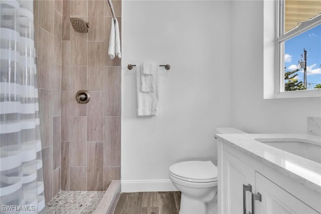 bathroom featuring vanity, toilet, baseboards, tiled shower, and wood finished floors