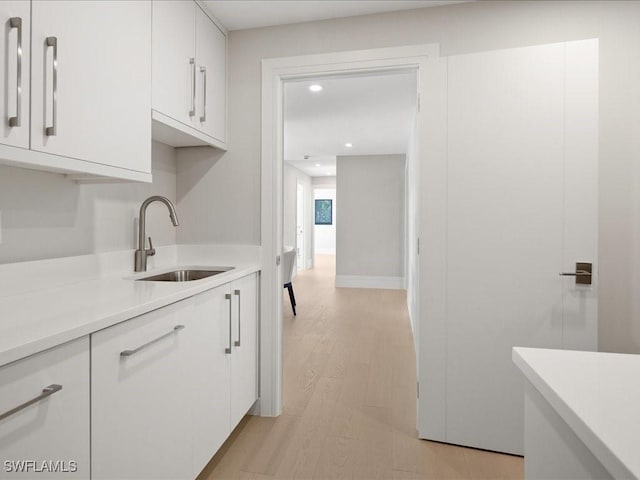 kitchen featuring recessed lighting, light wood-style floors, light countertops, a sink, and white cabinetry