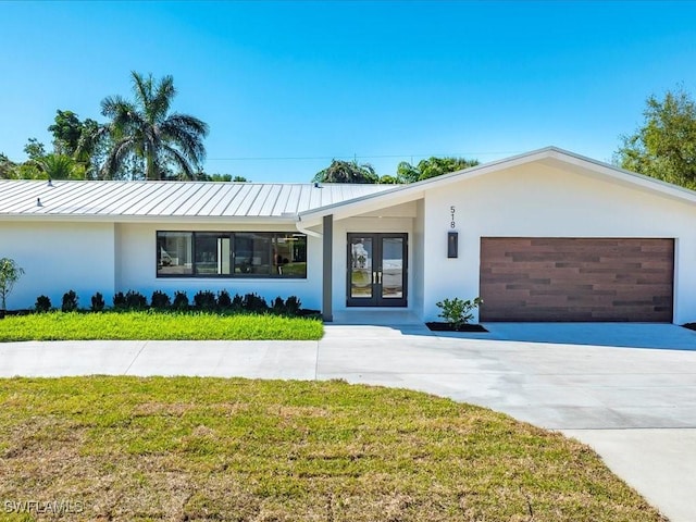 single story home with metal roof, an attached garage, stucco siding, french doors, and a front lawn