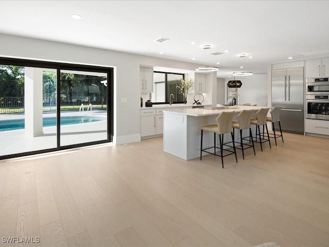 kitchen with white cabinets, appliances with stainless steel finishes, plenty of natural light, a center island, and light wood-type flooring