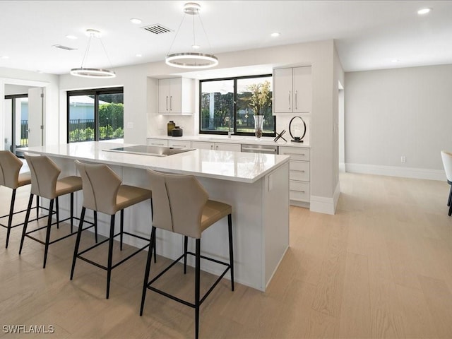kitchen featuring light wood finished floors, black electric stovetop, visible vents, light countertops, and hanging light fixtures