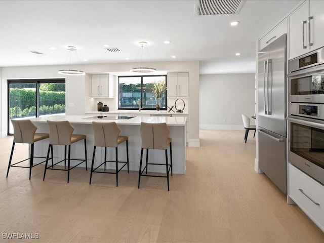 kitchen featuring white cabinets, appliances with stainless steel finishes, visible vents, light wood-style floors, and a center island
