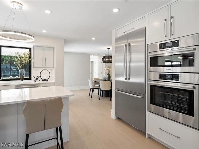 kitchen with recessed lighting, light wood finished floors, light stone countertops, tasteful backsplash, and appliances with stainless steel finishes