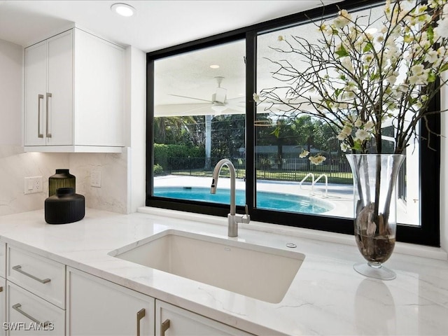 kitchen with tasteful backsplash, white cabinets, light stone countertops, and a sink