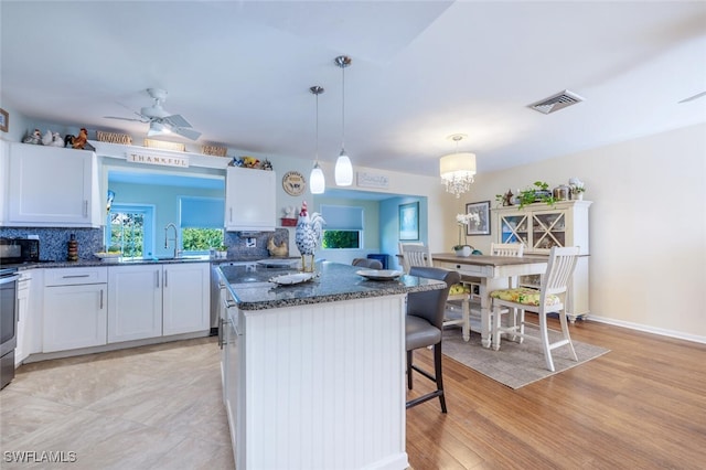 kitchen with visible vents, backsplash, a kitchen island, black microwave, and a breakfast bar