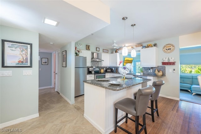 kitchen featuring decorative backsplash, white cabinetry, stainless steel appliances, and wall chimney exhaust hood