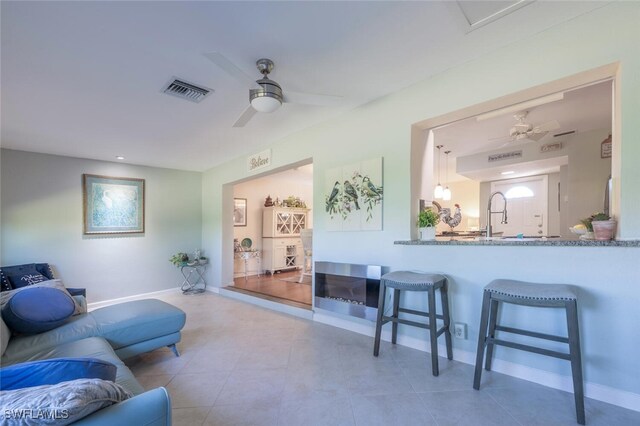 living area featuring tile patterned floors, visible vents, baseboards, and ceiling fan
