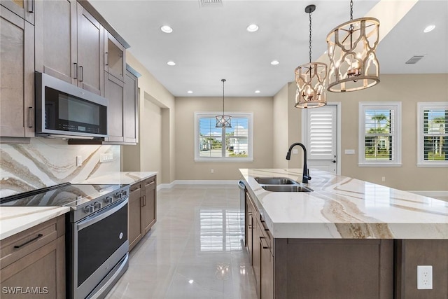 7282 Saona Ct, Naples, FL 34113 - kitchen with appliances with stainless steel finishes, a sink, a chandelier, a center island with sink, and light stone counters
