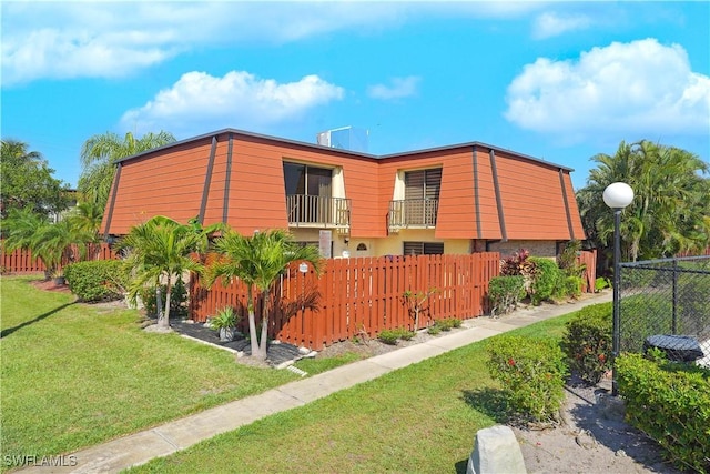 view of side of home with a balcony, a fenced front yard, and a yard