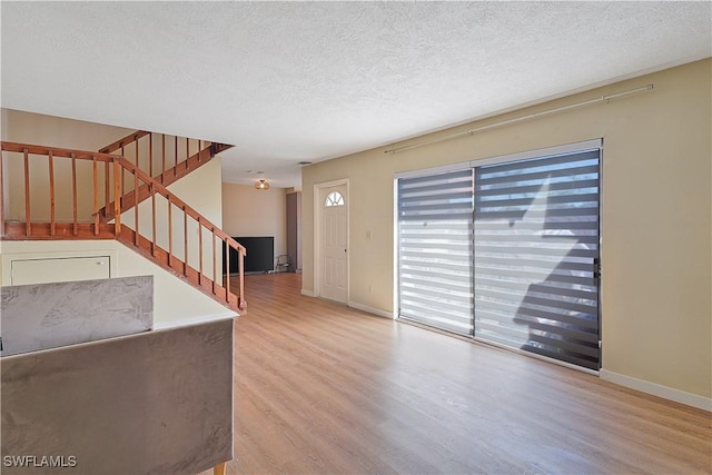 unfurnished living room with baseboards, a textured ceiling, stairway, and wood finished floors