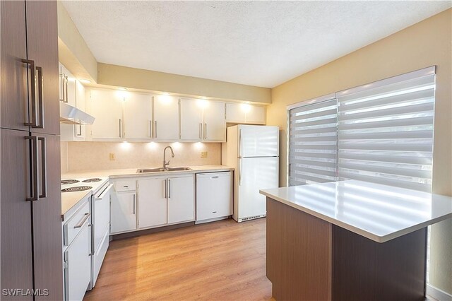 kitchen featuring light countertops, a sink, light wood finished floors, under cabinet range hood, and white appliances