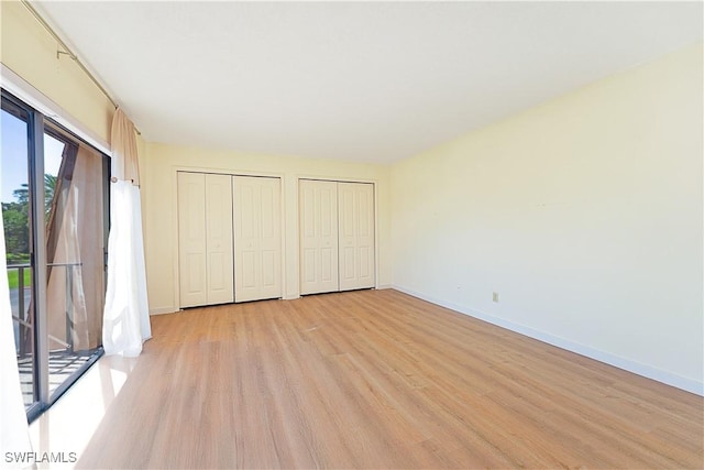 unfurnished bedroom featuring two closets, baseboards, light wood-style floors, and access to exterior