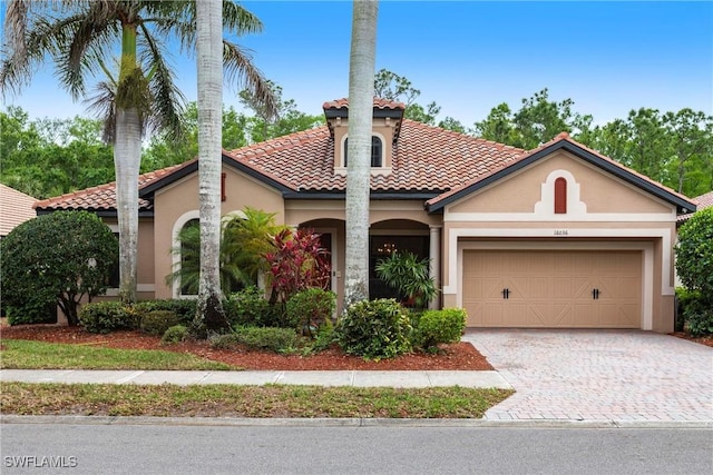 mediterranean / spanish-style home featuring stucco siding, an attached garage, and decorative driveway