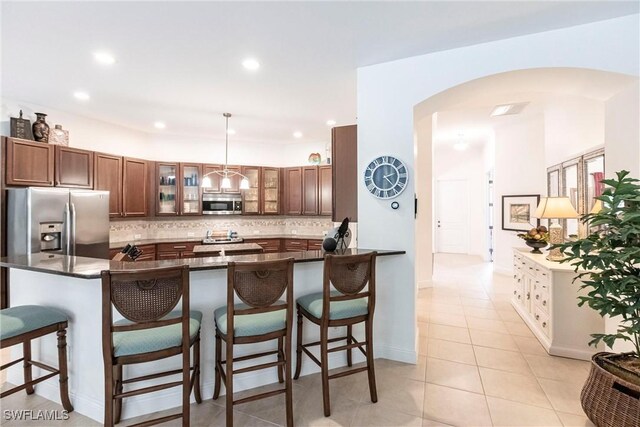 kitchen with stainless steel appliances, dark countertops, tasteful backsplash, arched walkways, and a breakfast bar area