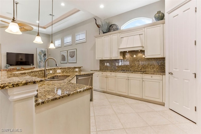 kitchen with a tray ceiling, backsplash, dark stone counters, a sink, and custom exhaust hood