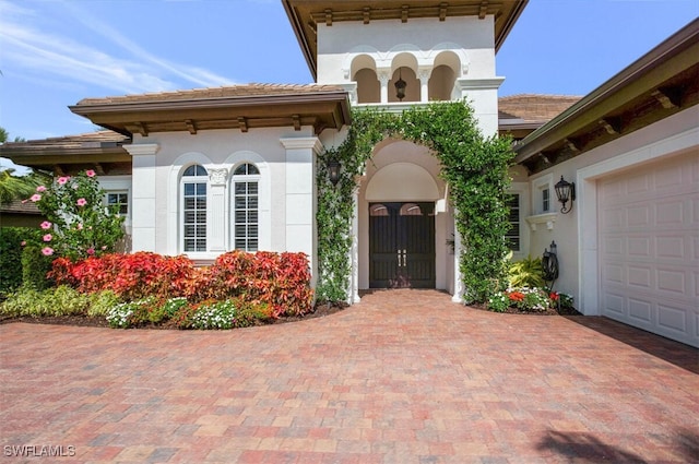 entrance to property featuring decorative driveway, a garage, and stucco siding
