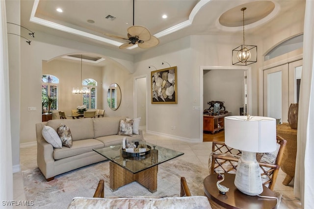 living area with light tile patterned flooring, a raised ceiling, ceiling fan with notable chandelier, visible vents, and arched walkways