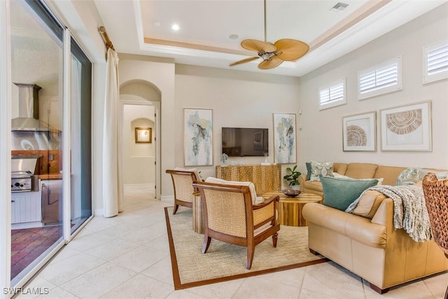 living area with light tile patterned floors, a raised ceiling, arched walkways, ceiling fan, and visible vents