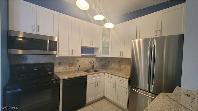 kitchen with light stone counters, white cabinets, black appliances, decorative backsplash, and a sink