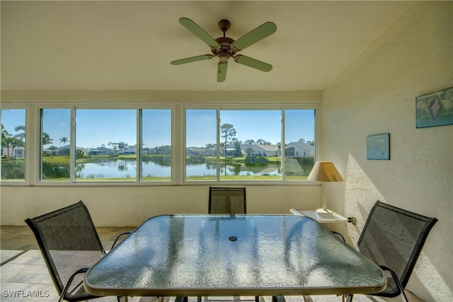 dining room featuring a textured wall, a water view, and ceiling fan