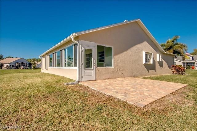 rear view of house featuring stucco siding, a patio, and a yard