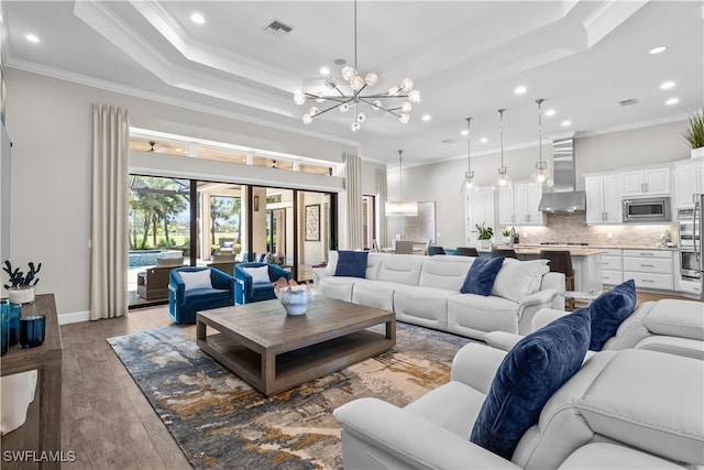 living room featuring a chandelier, ornamental molding, a raised ceiling, recessed lighting, and light wood-type flooring